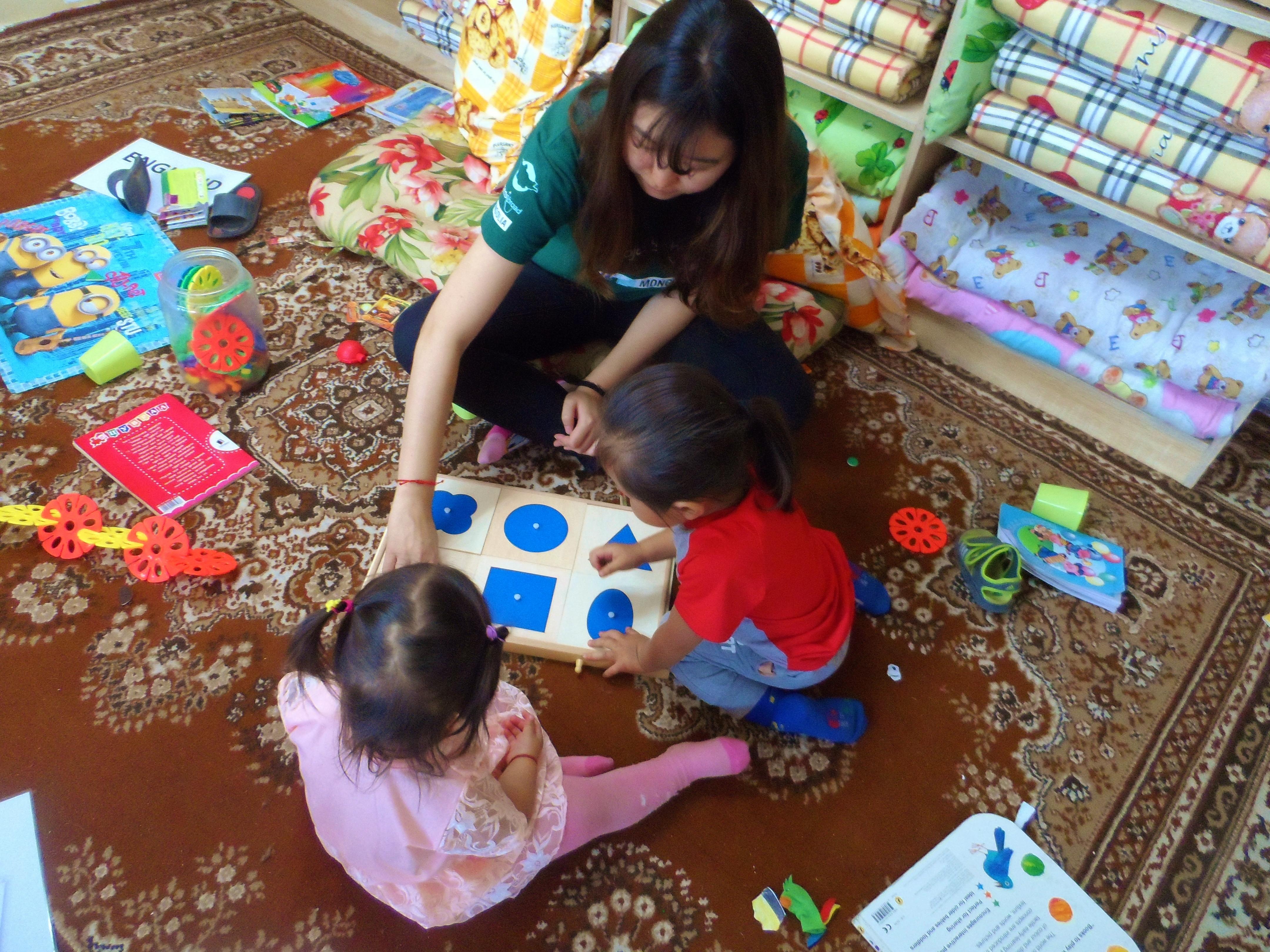 Female Childcare volunteer with children in Mongolia is teaching children basic shape games during a Care and Psychology internship. Projects Abroad Childcare volunteer teaches children shape games in a care centre during a Psychology work experience in Mongolia.
